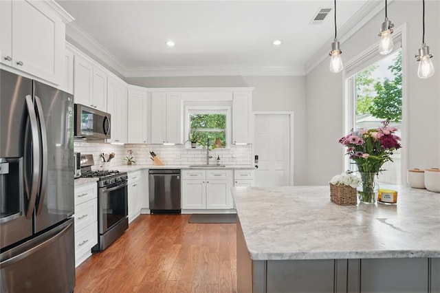 kitchen with appliances with stainless steel finishes, ornamental molding, wood finished floors, backsplash, and white cabinets