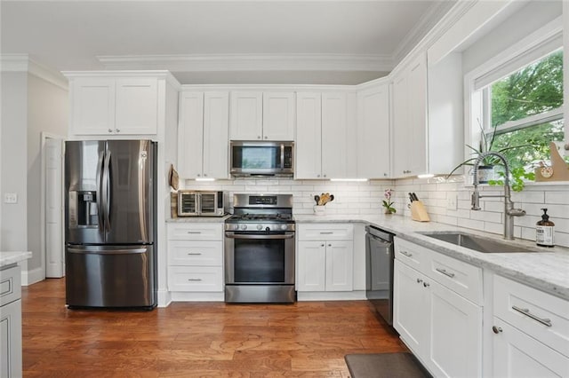 kitchen with stainless steel appliances, a sink, ornamental molding, wood finished floors, and white cabinets
