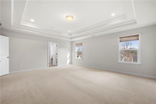 empty room featuring a raised ceiling, light carpet, baseboards, and ornamental molding