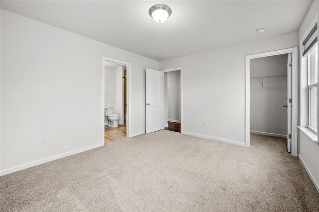 unfurnished bedroom featuring a spacious closet, baseboards, and carpet