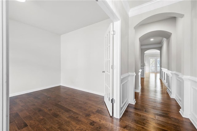 corridor featuring arched walkways, dark wood-type flooring, crown molding, and a decorative wall