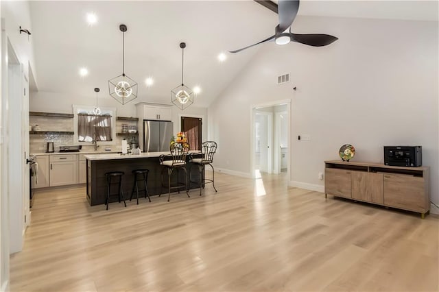 kitchen with a center island with sink, a breakfast bar, stainless steel refrigerator, hanging light fixtures, and white cabinets