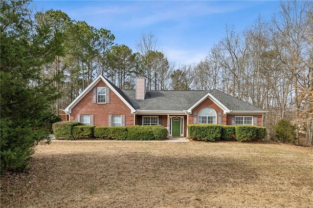 view of front of home with brick siding, a chimney, a front yard, and a shingled roof