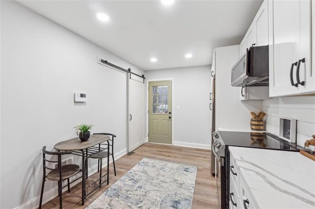 kitchen featuring a barn door, stainless steel appliances, white cabinets, light wood finished floors, and light stone countertops