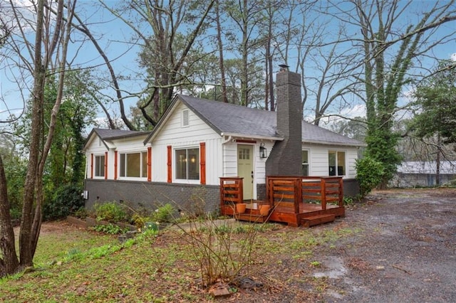 view of front of house featuring a wooden deck, brick siding, a chimney, crawl space, and board and batten siding