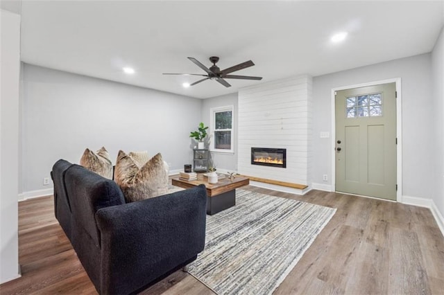 living room with ceiling fan, wood finished floors, baseboards, and a large fireplace