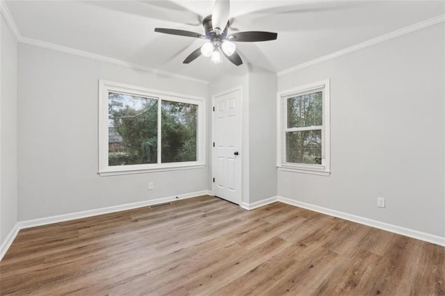 empty room featuring visible vents, crown molding, baseboards, and wood finished floors