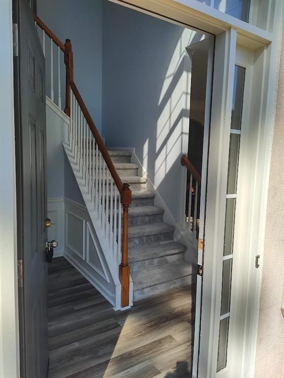 stairway featuring a decorative wall, wood finished floors, and a wainscoted wall