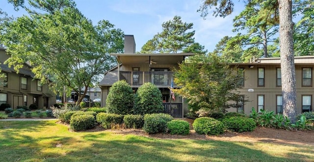 view of front of property with a front yard, a chimney, ceiling fan, and a balcony
