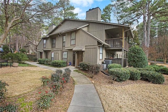 view of front of property with cooling unit, a chimney, ceiling fan, and a balcony