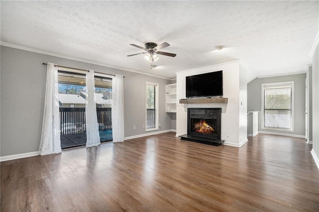unfurnished living room featuring ceiling fan, a lit fireplace, baseboards, ornamental molding, and wood finished floors
