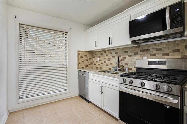 kitchen with decorative backsplash, appliances with stainless steel finishes, white cabinets, a sink, and baseboards