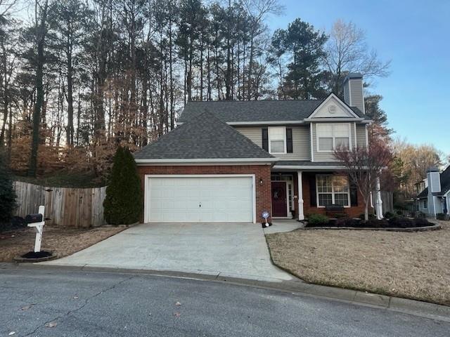 traditional home featuring brick siding, fence, a chimney, driveway, and an attached garage