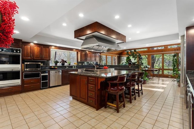 kitchen with dark stone countertops, appliances with stainless steel finishes, light tile patterned floors, an island with sink, and a breakfast bar area