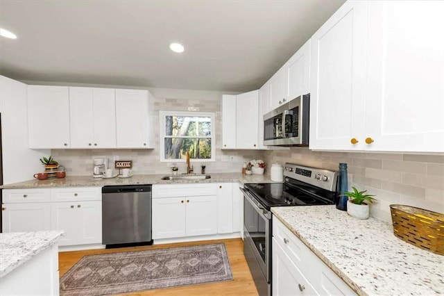 kitchen featuring sink, tasteful backsplash, light hardwood / wood-style flooring, white cabinets, and appliances with stainless steel finishes