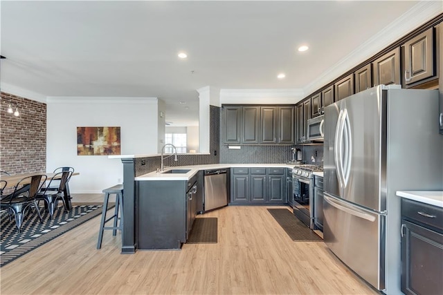 kitchen with sink, a breakfast bar area, ornamental molding, appliances with stainless steel finishes, and backsplash