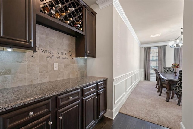 kitchen featuring dark brown cabinets, dark stone countertops, ornamental molding, and pendant lighting