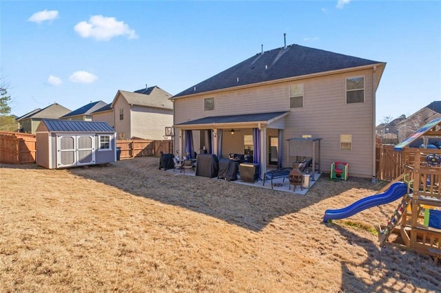 back of house featuring a playground, a shed, an outdoor fire pit, and a patio