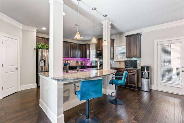 kitchen with a kitchen bar, an island with sink, appliances with stainless steel finishes, hanging light fixtures, and light stone countertops