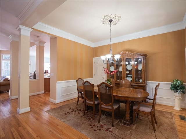 dining area with a notable chandelier, hardwood / wood-style flooring, decorative columns, and crown molding