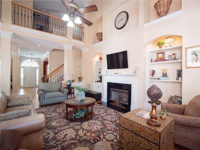 living room featuring built in features, decorative columns, a towering ceiling, and ceiling fan