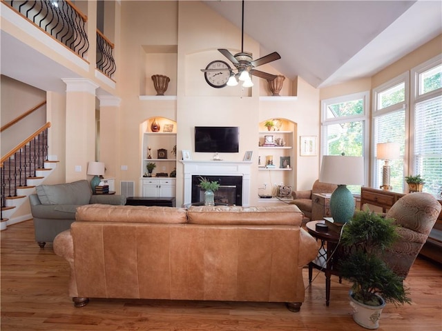 living room with hardwood / wood-style floors, high vaulted ceiling, built in shelves, and ceiling fan