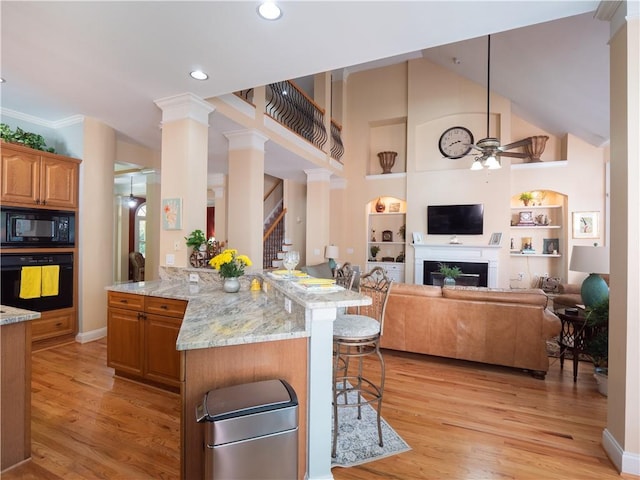 kitchen featuring a kitchen breakfast bar, decorative columns, black appliances, and light hardwood / wood-style floors