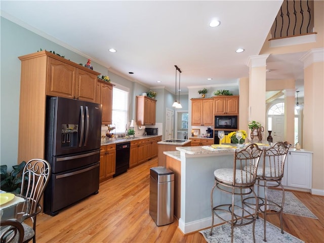 kitchen featuring decorative columns, crown molding, black appliances, and light hardwood / wood-style flooring