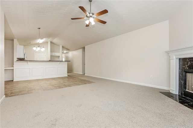 unfurnished living room with lofted ceiling, light colored carpet, a high end fireplace, baseboards, and ceiling fan with notable chandelier