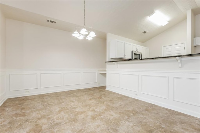 kitchen with visible vents, dark countertops, stainless steel microwave, an inviting chandelier, and vaulted ceiling