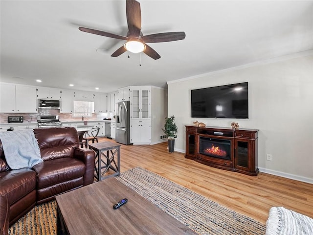 living room with ornamental molding, ceiling fan, and light wood-type flooring