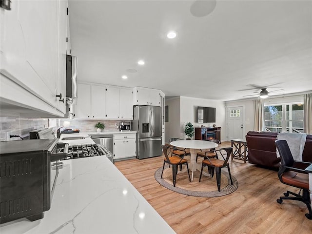 kitchen featuring light stone counters, white cabinetry, appliances with stainless steel finishes, light hardwood / wood-style floors, and backsplash