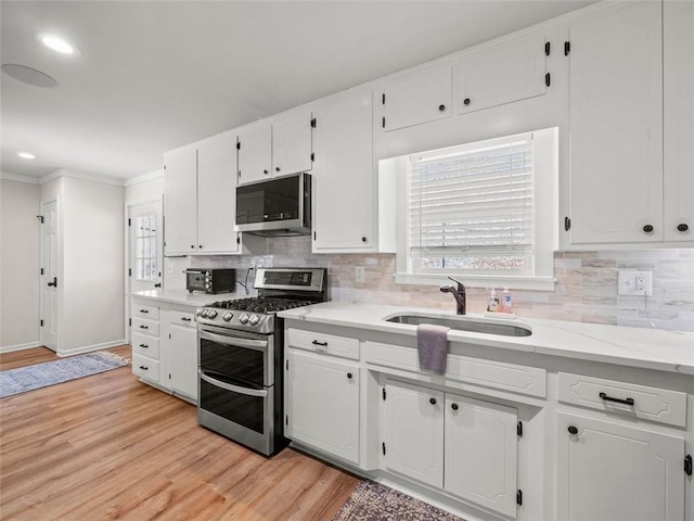 kitchen featuring appliances with stainless steel finishes, white cabinetry, sink, decorative backsplash, and light hardwood / wood-style floors