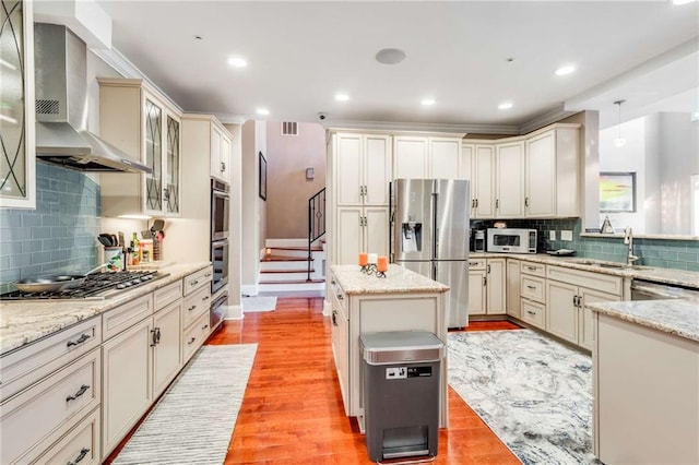 kitchen with tasteful backsplash, a kitchen island, stainless steel appliances, light hardwood / wood-style floors, and wall chimney exhaust hood