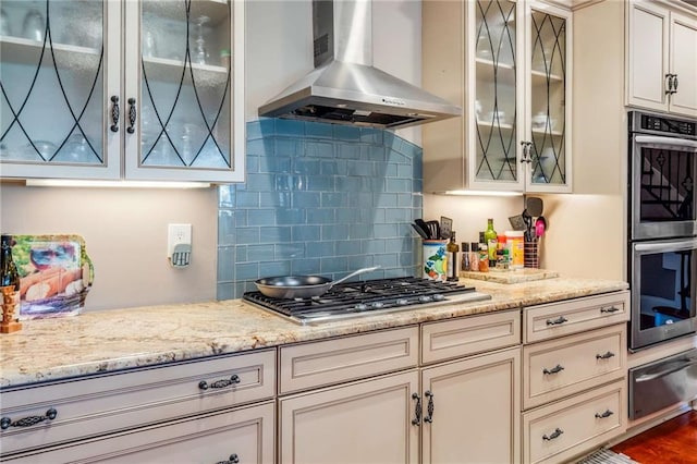 kitchen with stainless steel appliances, wall chimney range hood, backsplash, dark hardwood / wood-style floors, and light stone countertops