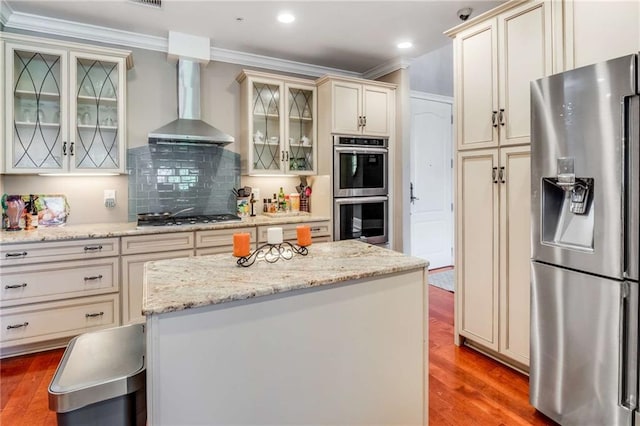 kitchen featuring hardwood / wood-style floors, a center island, appliances with stainless steel finishes, and wall chimney range hood