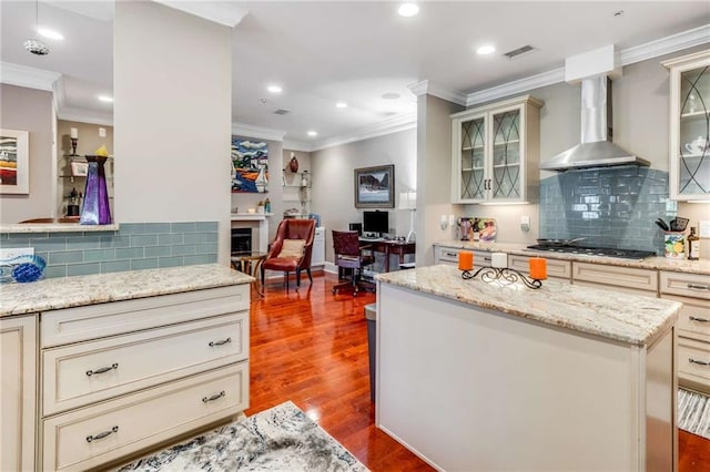 kitchen featuring hardwood / wood-style flooring, tasteful backsplash, wall chimney range hood, crown molding, and a kitchen island