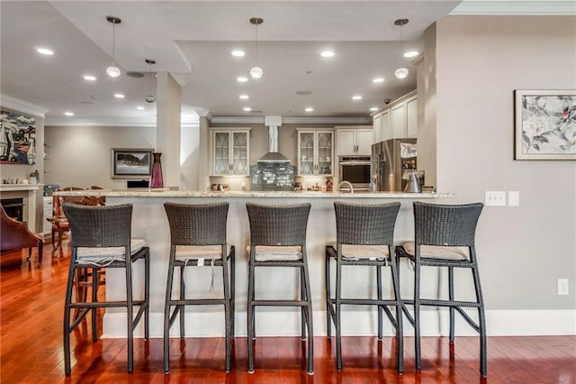 kitchen with hanging light fixtures, appliances with stainless steel finishes, dark hardwood / wood-style floors, and wall chimney exhaust hood