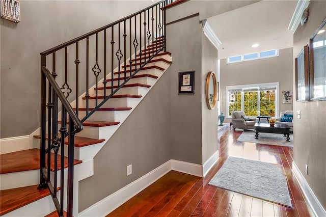 stairway featuring dark hardwood / wood-style floors, a towering ceiling, and crown molding