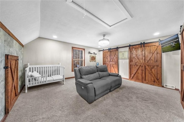 carpeted bedroom with visible vents, attic access, vaulted ceiling, a textured ceiling, and a barn door