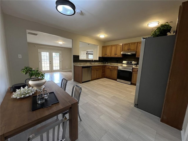 1929 Hazelwood Dr SE, Marietta, GA 30067 - kitchen featuring appliances with stainless steel finishes, under cabinet range hood, brown cabinets, tasteful backsplash, and french doors