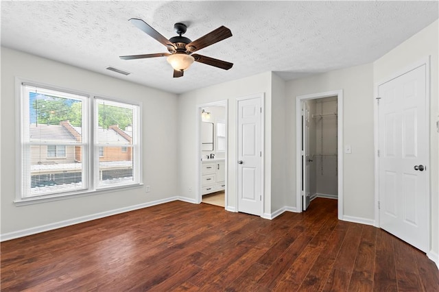unfurnished bedroom featuring dark wood-style flooring, baseboards, a textured ceiling, connected bathroom, and a walk in closet