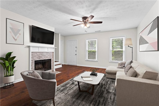 living room featuring wood finished floors, a ceiling fan, a fireplace, baseboards, and a textured ceiling