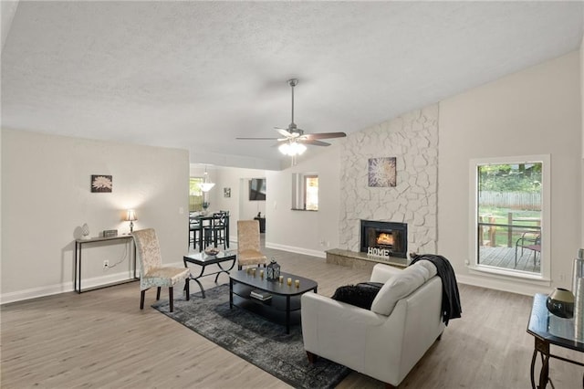 living room with a stone fireplace, hardwood / wood-style floors, ceiling fan, and a textured ceiling