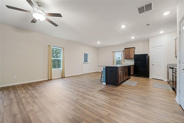 kitchen featuring a kitchen breakfast bar, a kitchen island with sink, black refrigerator, and light hardwood / wood-style flooring