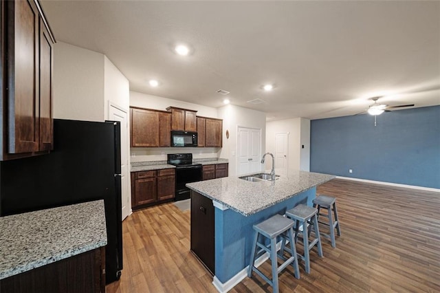 kitchen with sink, an island with sink, light hardwood / wood-style floors, a breakfast bar, and black appliances