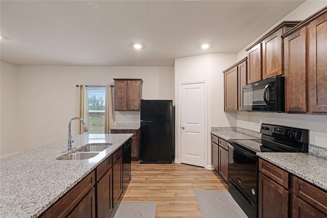 kitchen featuring light stone countertops, sink, light hardwood / wood-style floors, and black appliances