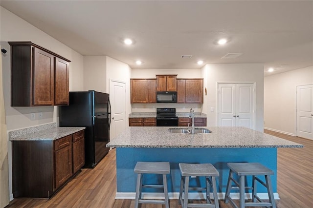 kitchen featuring black appliances, sink, an island with sink, light hardwood / wood-style floors, and light stone counters