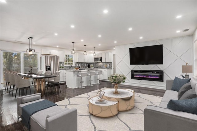 living area featuring recessed lighting, visible vents, dark wood-type flooring, and a glass covered fireplace