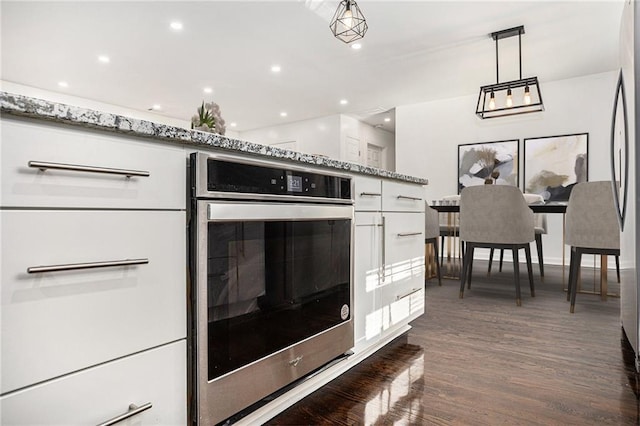 kitchen featuring dark wood-type flooring, light stone countertops, stainless steel oven, hanging light fixtures, and white cabinetry